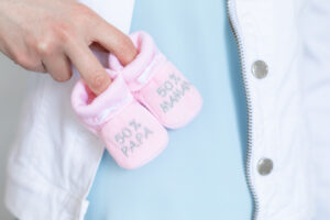 young pregnant woman with baby booties in hands - 50% Dad 50% Mum - Gender reveal